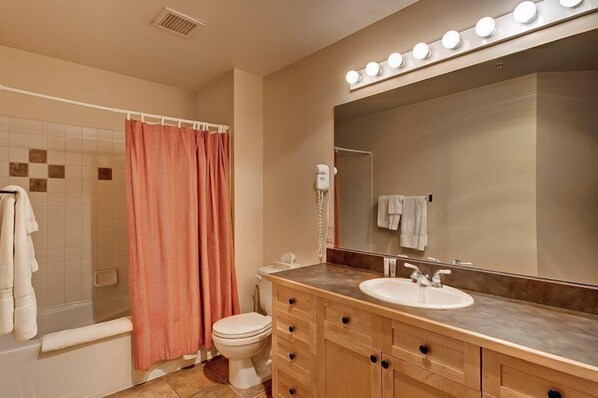 Une salle de bain comprenant une douche, des toilettes, un meuble-lavabo avec un évier et un grand miroir avec des lumières au-dessus.