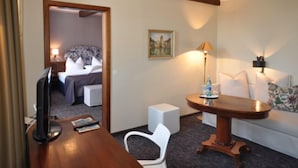 Una camera d'albergo con una scrivania in legno, una televisione, un tavolino con una lampada, una sedia bianca e un letto con copripiumino floreale.
