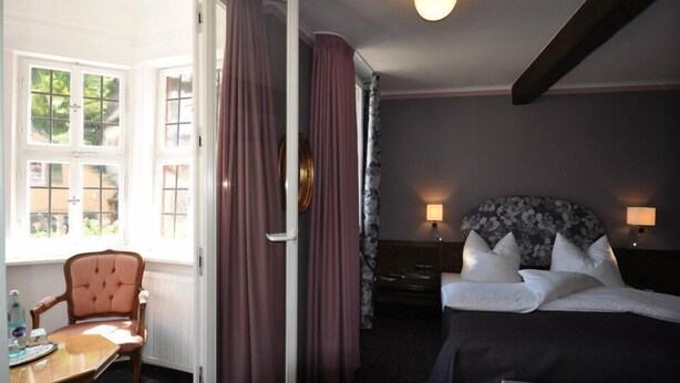 Una camera d'albergo con un letto, comodini, una sedia e una finestra con tende.