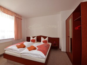 Una habitación de hotel con una cama grande, un armario y un ventanal con cortinas.