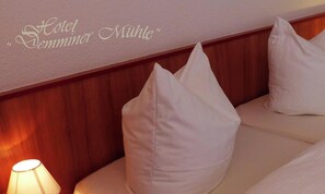 A hotel room with a wall-mounted sign reading 'Hotel Demminer Mühle' and a bed with white pillows and a beige headboard.
