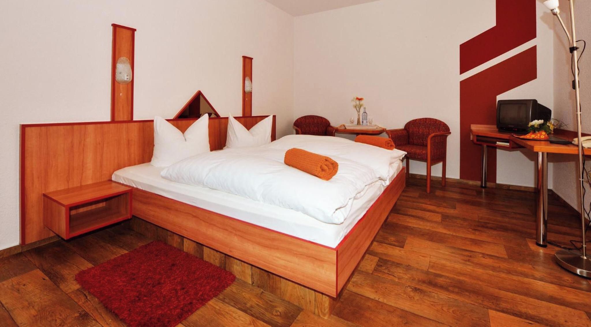 A hotel room with a wooden bed, a red rug, a desk with a television, and a chair.