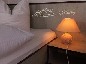 A hotel room with a bed, a nightstand with a lamp, and a wall sign that reads 'Hotel Semminger Mühle'.