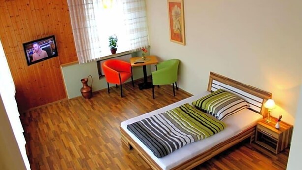 Een kamer met een bed, een televisie, een raam met gordijnen, een klein tafeltje en twee stoelen.