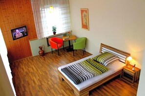 Una habitación con una cama, televisión, ventana con cortinas, una mesita y dos sillas.