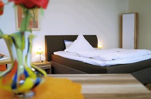 Una habitación de hotel con una cama, una mesita de noche, una lámpara, un espejo y un jarrón con flores.