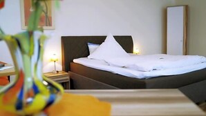 Een hotelkamer met een bed, nachtkastje, lamp, spiegel en een vaas met bloemen.
