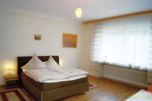 A bedroom with a bed, bedside lamps, a window with blinds, and a small picture on the wall.