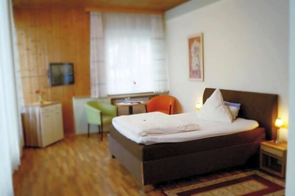 Un dormitorio con cama, escritorio, silla y un pequeño armario.