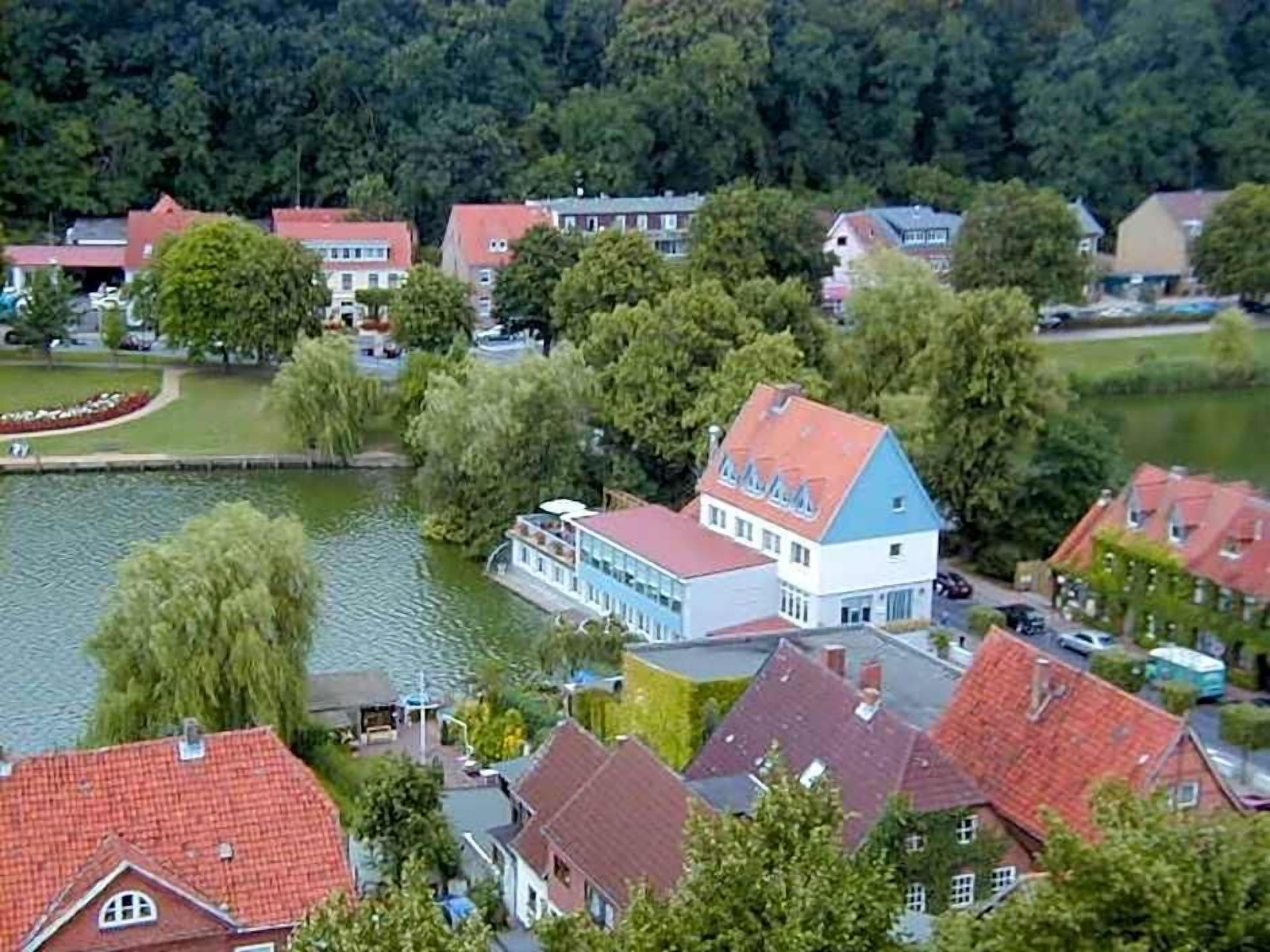Ein Wohngebiet am Seeufer mit Häusern, einem markanten Gebäude mit blauem Dach und einem Fluss.