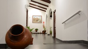 Um corredor com um grande vaso de terracota, plantas em vasos, um quadro na parede e uma escadaria.