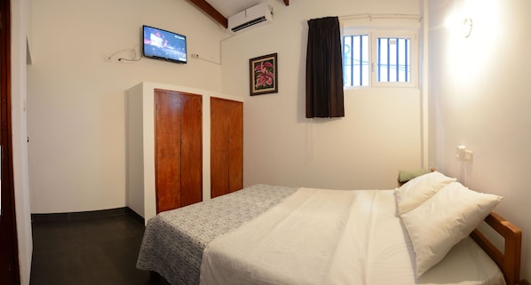 Un dormitorio con cama, armario, televisor y ventana con cortinas.