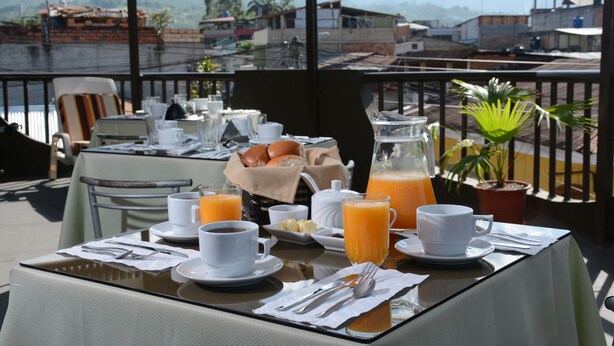 Mesa de café da manhã posta com xícaras, jarra de suco de laranja e um prato de pão.