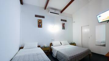 Habitación de hotel con dos camas, un televisor montado en la pared y una mesa de madera.
