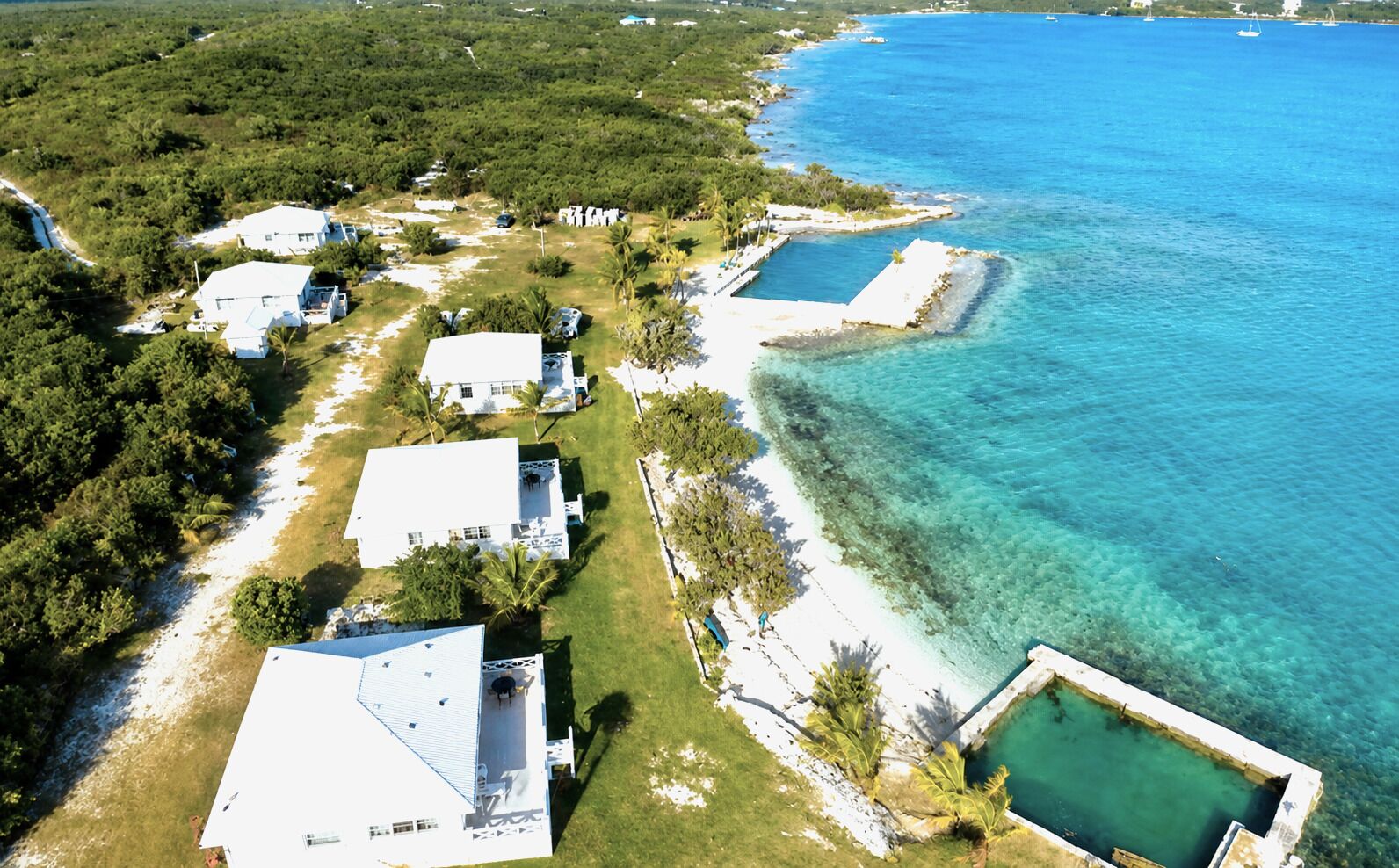 An aerial view of a coastal property with multiple white buildings, clear blue waters, and a small pool.