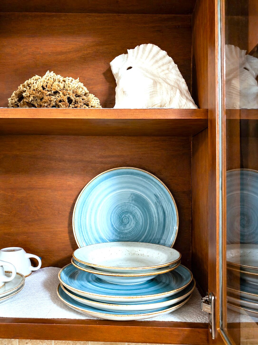Een houten kast met planken, gevuld met keramieken servies en een wit decoratief object.