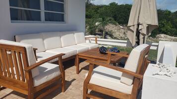 A patio with a white sofa, wooden chairs, and a table.