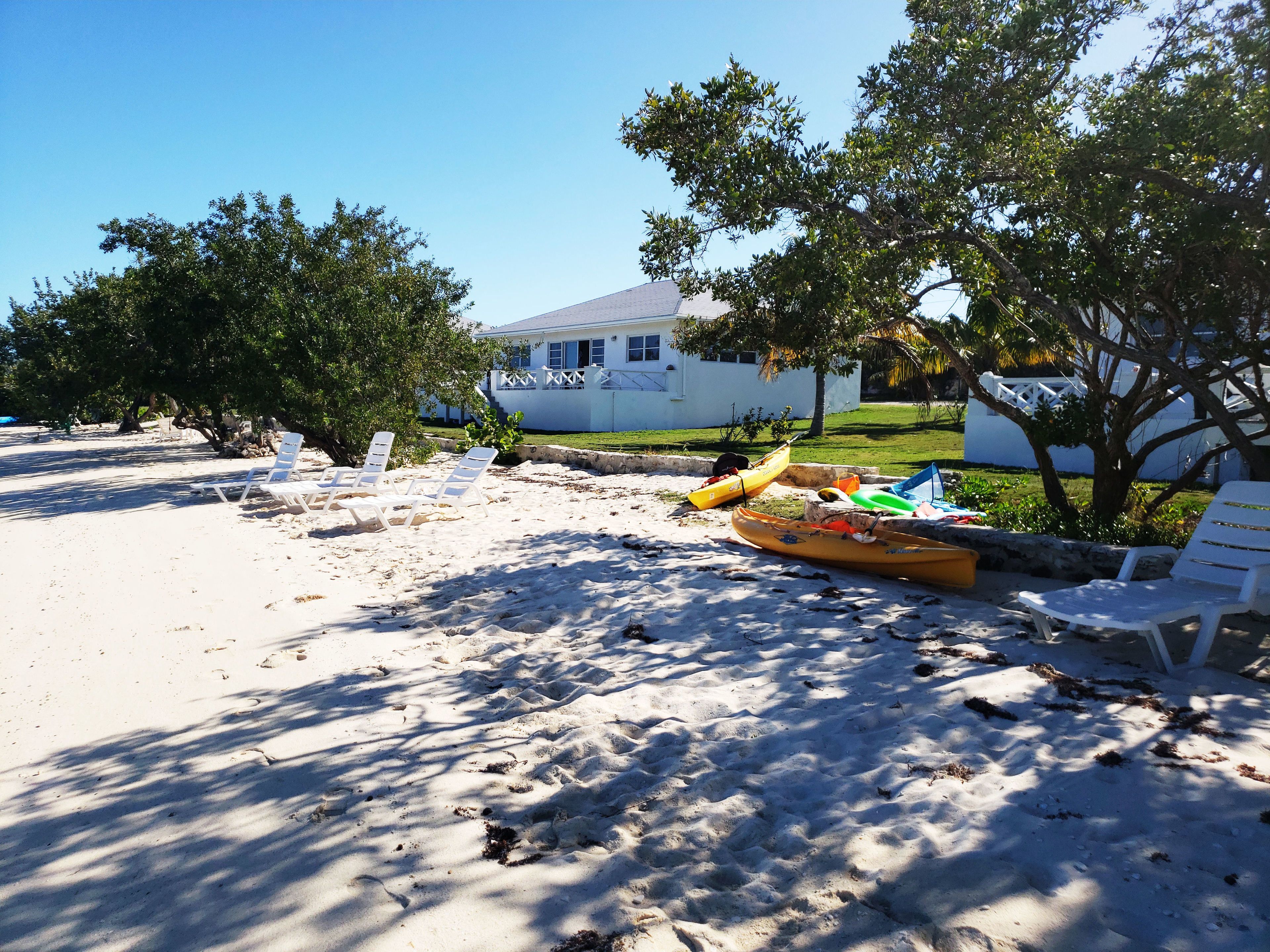 A sandy beach with white lounge chairs, a yellow kayak, and a white building in the background.