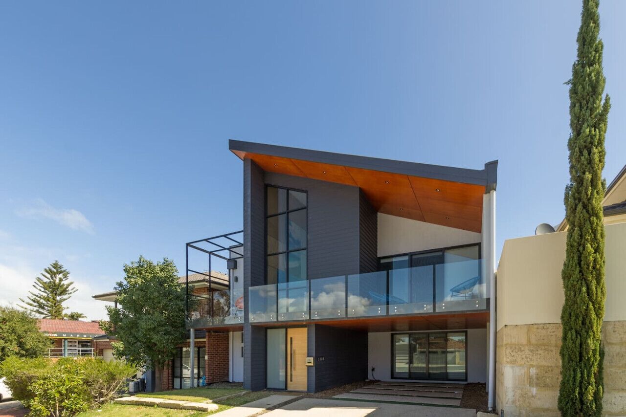 A modern two-story house with large glass windows, a wooden deck, and a brick facade.