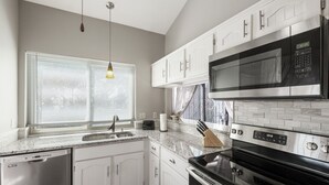 Una cocina moderna con armarios blancos, lavavajillas de acero inoxidable, microondas y estufa.
