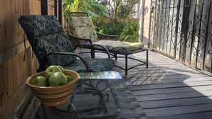 Un espacio al aire libre techado con sillas de mimbre y una mesa de vidrio, un cuenco de manzanas verdes y una valla de madera al fondo.