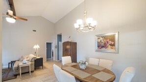 Un comedor con una mesa de madera, sillas blancas, una araña y un cuadro en la pared.