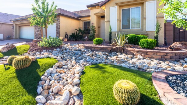 Una casa residencial con fachada de piedra, un garaje y un jardín delantero bien cuidado con rocas, césped y cactus.