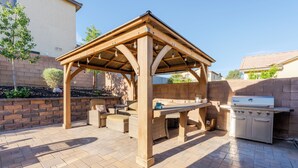 Un patio al aire libre con una pérgola de madera, una parrilla y asientos.