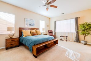 Quarto com cama, mesas de cabeceira, ventilador de teto, janela com persianas, planta em vaso e vista para o exterior.