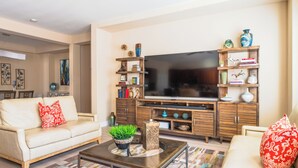 Una sala de estar con sofá, mesa de centro, televisor, aparador de madera y objetos decorativos.