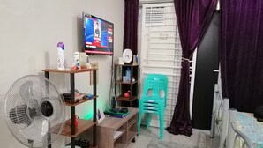 Una habitación pequeña y ordenada con televisión, ventilador, escritorio y silla.