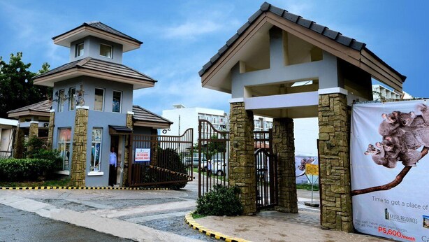 Un complejo residencial con portón, fachada de piedra y entrada cubierta, con un anuncio de una propiedad en venta.