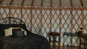A cozy interior with a bed, ottomans, a small table, and a ceiling fan. - Luxury Yurts on Lake Grapevine  (Southlake)