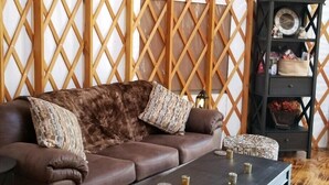 A cozy living area with a brown leather sofa, a coffee table, and a bookshelf against a wooden lattice wall. - Luxury Yurts on Lake Grapevine  (Southlake)