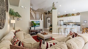 A spacious living room with a large sofa, a television, and a kitchen area in the background.