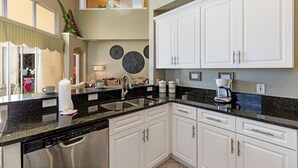 A modern kitchen with white cabinets, a black countertop, stainless steel appliances, and decorative wall art.