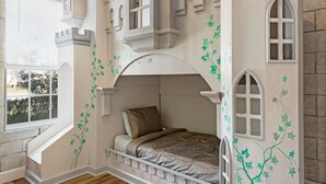 A bedroom with a castle-themed design, including a bed, windows, and a ceiling fan.