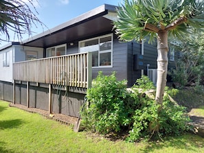 A modern two-story house with a balcony, a garden with various plants, and a palm tree. - Magical West Coast Retreat (Bethells Beach)