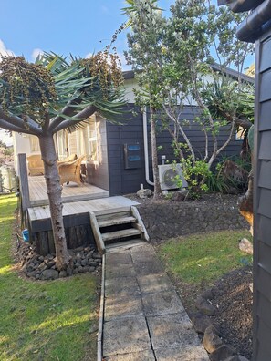 A residential property with a wooden deck, a stone pathway, and a variety of plants. - Magical West Coast Retreat (Bethells Beach)