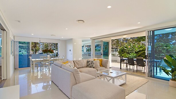 A modern living room with a sectional sofa, a glass coffee table, and a dining area with chairs and a table.