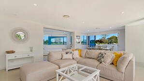 A modern living room with a beige sofa, a glass coffee table, and a view of a cityscape through large windows.