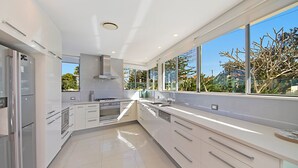 A modern kitchen with white cabinetry, stainless steel appliances, and large windows offering a view of the outdoors.