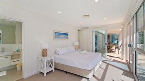 A modern bedroom with a bed, a bedside table, a lamp, a large window, and a view of the outside.