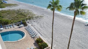 A beach view with a swimming pool, lounge chairs, and palm trees. - Beachcomber unit 504 (Longboat Key)