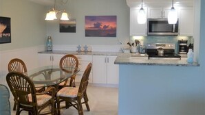 A modern kitchen with a glass dining table, white cabinets, and pendant lighting. - Beachcomber unit 504 (Longboat Key)