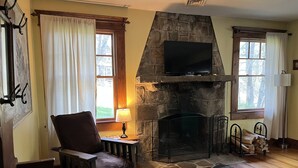 A cozy living room with a stone fireplace, a comfortable chair, a sofa, and a television mounted above the fireplace. - Lehigh Lodge Waterfront- Feat. in Philadelphia Mag. Gorgeous private waterfall! (Blakeslee)