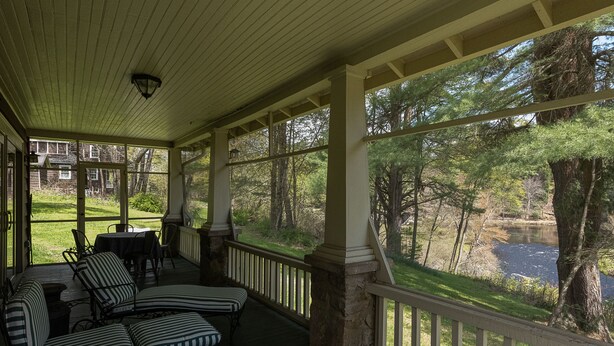 A covered porch with striped chairs and a table, overlooking a pond and trees. - Lehigh Lodge Waterfront- Feat. in Philadelphia Mag. Gorgeous private waterfall! (Blakeslee)