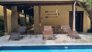 Et poolområde med flet loungesenge, et bord og en flisebelagt pool.