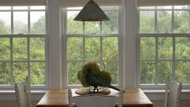 Una mesa de comedor con una escultura de un ave y una lámpara colgante en una habitación con ventanas amplias.
