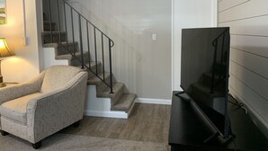A living room with a staircase, a sofa, and a television. - The Folly Jewel -  Sleeps 6 (Folly Beach)